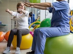 Ein Mann und ein kleines Mädchen führen in einem Trainingsbereich spielerisch Übungen mit Gymnastikbällen durch.