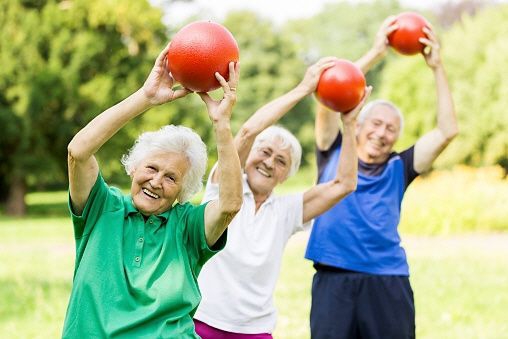 Drei ältere Frauen spielen mit roten Bällen im Freien, wobei alle lächeln und sportlich wirken.