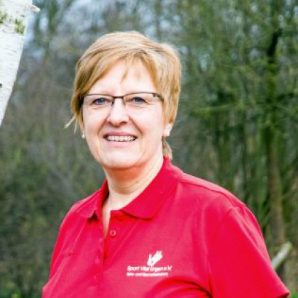 Porträt einer lächelnden Frau mittleren Alters vor einem Hintergrund aus Bäumen und einem Birkenstamm.