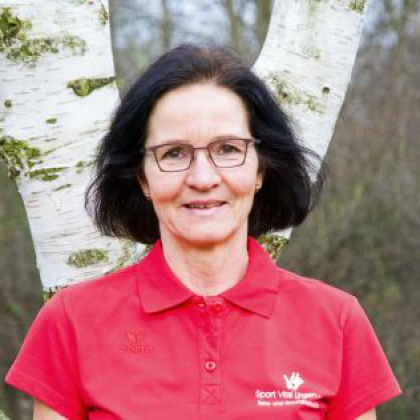 Porträt einer Frau in Brille, die vor einem Hintergrund aus Birkenbäumen posiert.